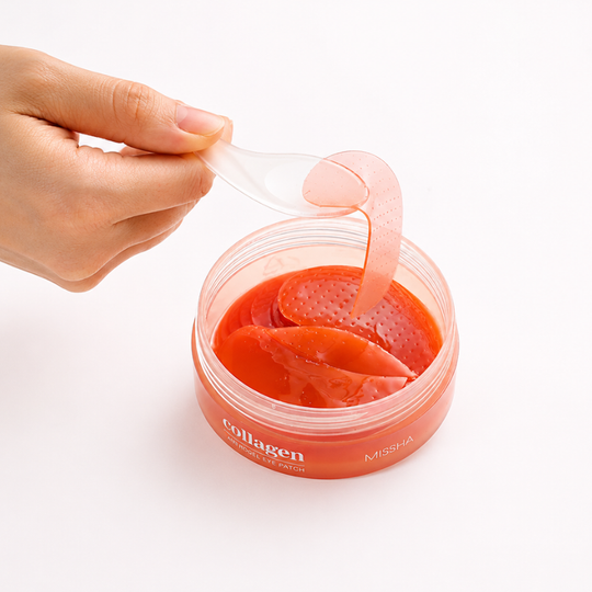 A hand holds a translucent spatula above an open round jar of red collagen eye patches on a clean white background.