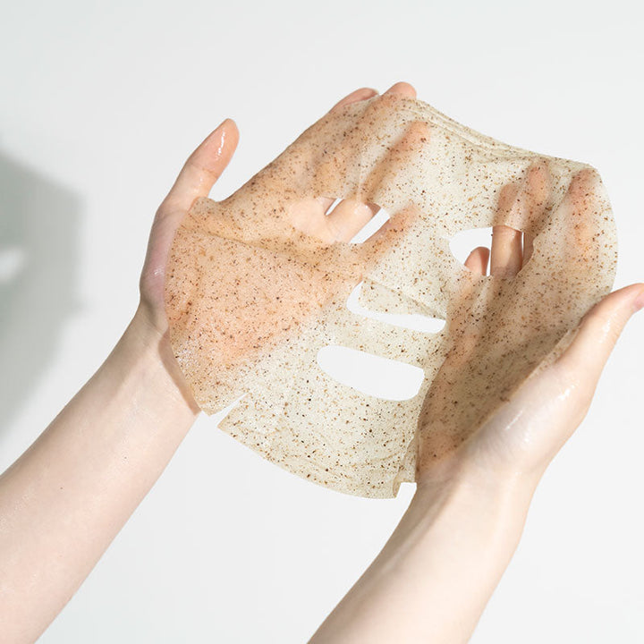 Two hands holding a beige exfoliating scrub against a light background